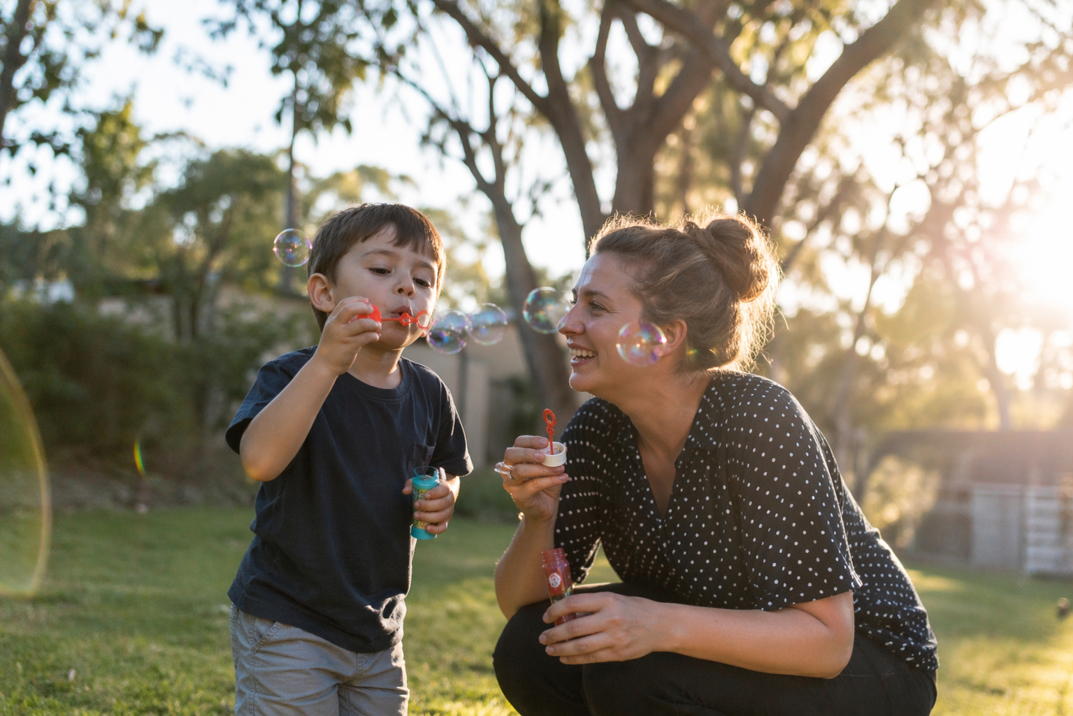 A therapist and a laughing child play outdoors with bubbles — a warm, candid speech therapy moment.